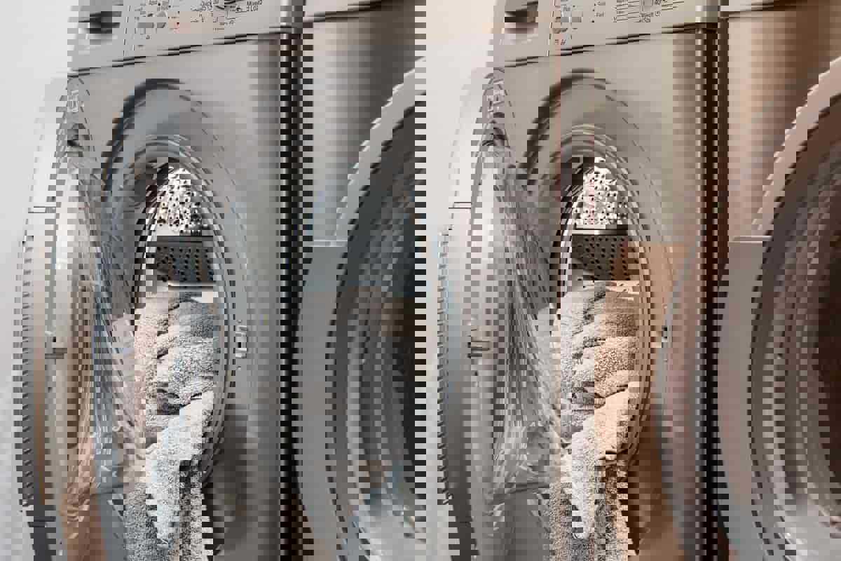 En sølvfarvet vaskemaskine. Der ligger et håndklæde i maskinen, som lågen ikke er lukket på endnu.